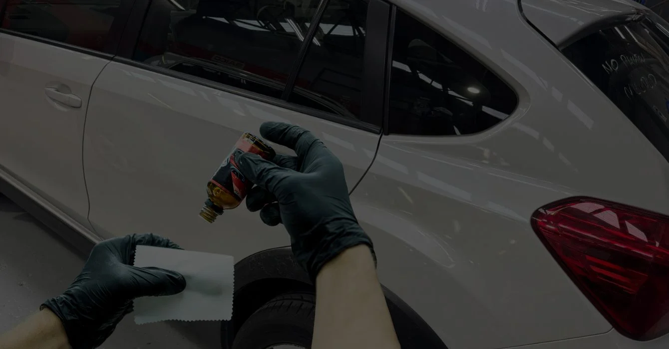 An auto repair expert conducts a final inspection, holding a microfiber cloth and detailing solution to ensure a flawless finish on the repaired vehicle.