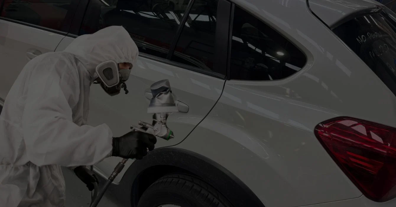 An auto technician applies paint to a previously repaired section of a vehicle, completing the refinishing process for a smooth, color-matched finish.